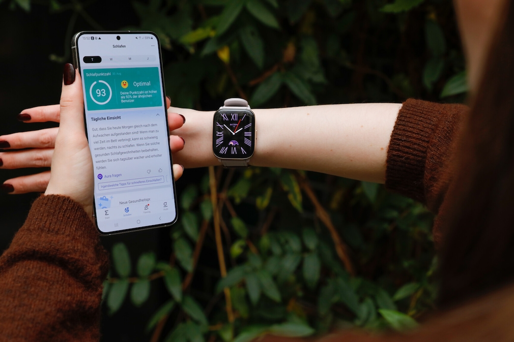 Amazfit Active am Handgelenk einer Person. Auf dem Display ist das Watchface zu sehen. Daneben hält sie ein Smartphone mit der Zepp-App. Dort sind die Schlafdaten zu sehen.