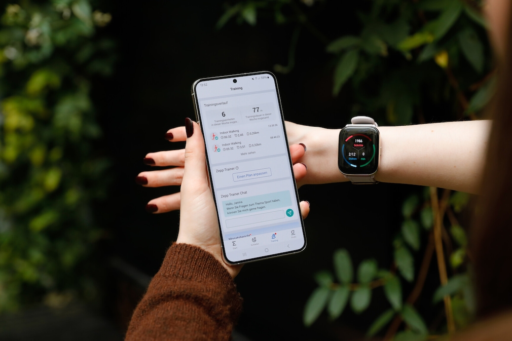 Amazfit Active am Handgelenk einer Person. Auf dem Display sind die Fitnessdaten zu sehen. In der linken Hand hält sie ein Smartphone mit der Zepp-App, welche die Trainingsdaten zeigt.