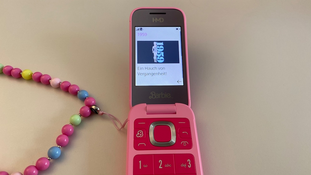 Barbie Phone aufgeklappt liegend auf einem weißen Untergrund. Auf dem Display sind Infos über die erste Barbie aus 1959 zu lesen.