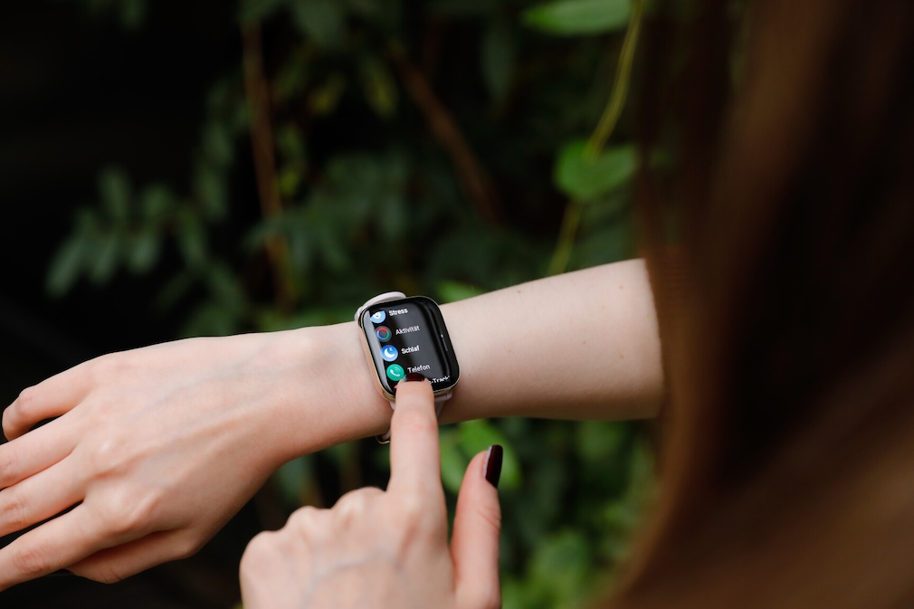 Über die Schulter fotografiert. Amazfit Active am Handgelenk einer Person. Auf dem Display ist das Menü mit den Punkten Stress, Aktivität, Schlaf und Telefon zu sehen. Die linke Hand bedient die Uhr.